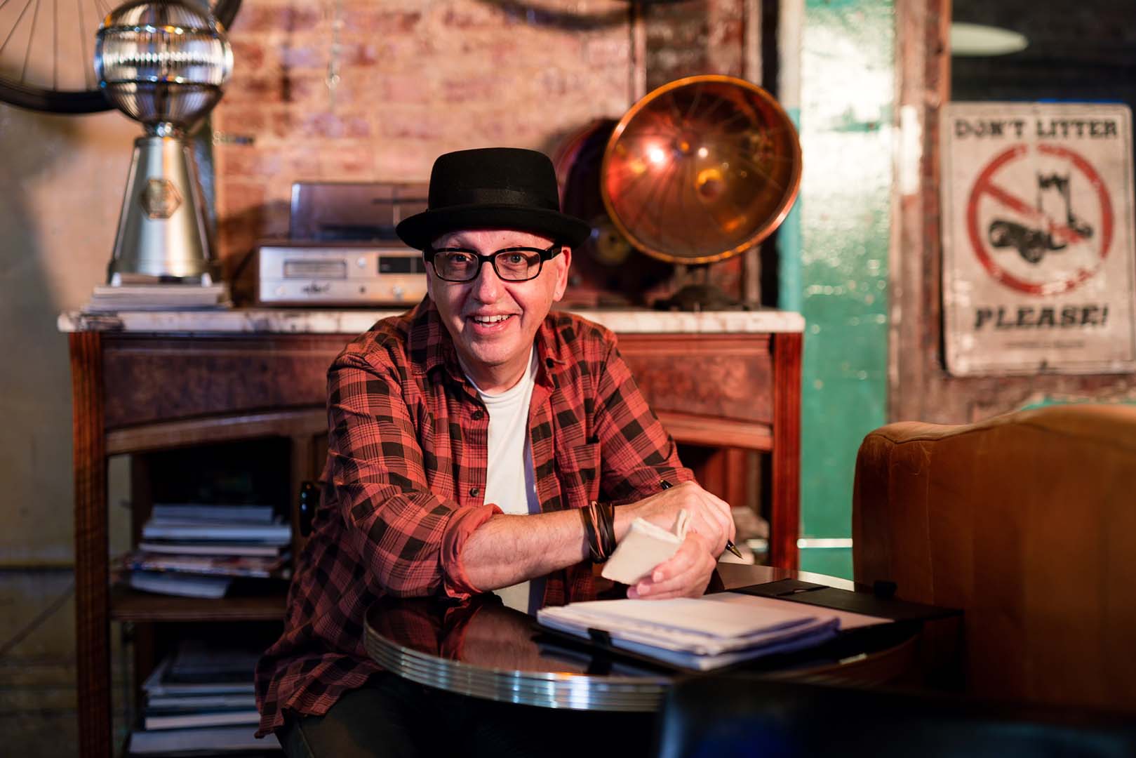 Sandy in a black hat and red plaid shirt, smiling across a table